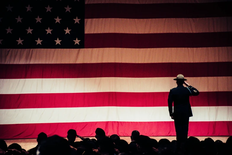 a man standing in front of an american flag, unsplash, symbolism, on the stage, miltary, audience, ( ( theatrical ) )