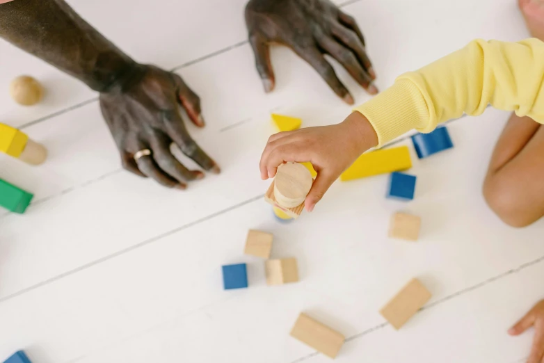 a group of children playing with blocks on a floor, by Arabella Rankin, pexels contest winner, visual art, single pair of hands, on a yellow canva, dust and scratches, on a white table