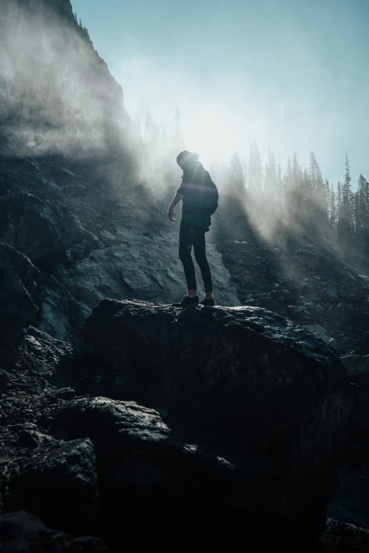 a person standing on a rock in the mountains, inspired by Michael Komarck, pexels contest winner, strong eerie back light, paul barson, struggling, backfacing