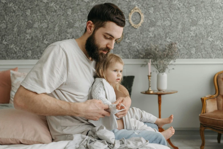 a man and a little girl sitting on a bed, pexels contest winner, visual art, bearded, nursing, looking serious, playing games