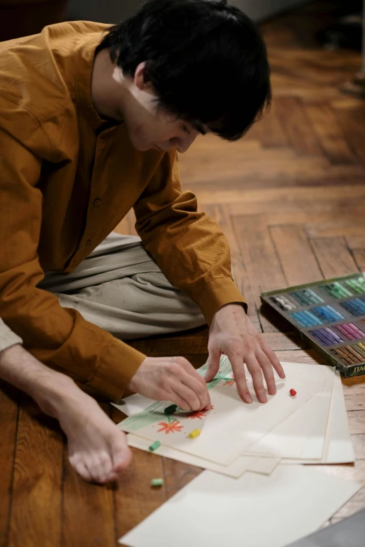 a man sitting on the floor working on a piece of paper, by artist, pexels contest winner, visual art, traditional japanese colors, hammershøi, crayons on paper, album cover