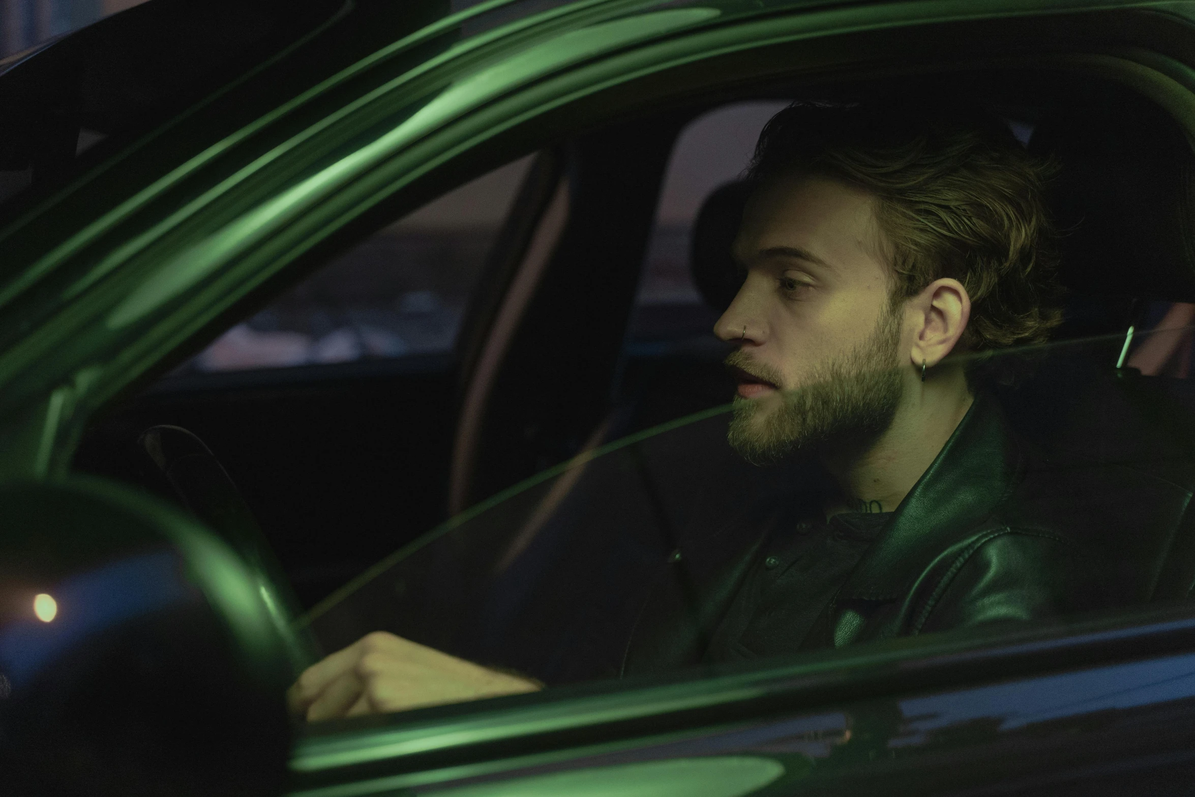 a man sitting in the passenger seat of a car, an album cover, inspired by Elsa Bleda, trending on pexels, photorealism, green lights, charlie cox, movie action still frame, official music video