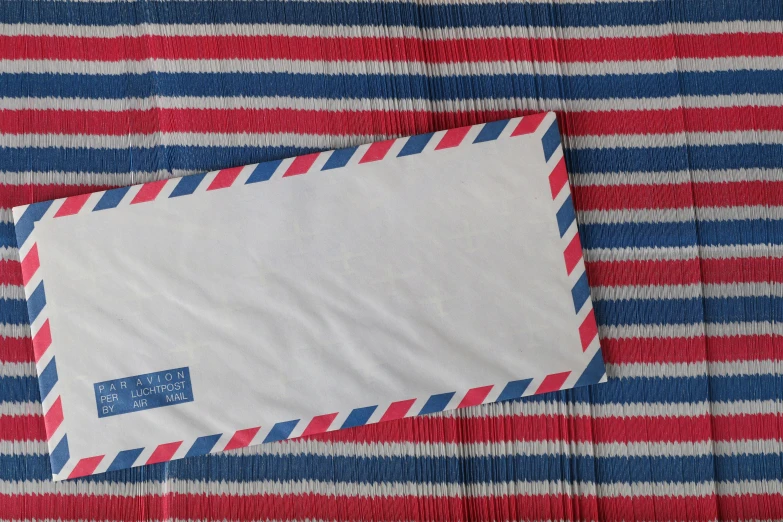 an envelope sitting on top of a red, white and blue blanket, inspired by Bridget Riley, unsplash, mail art, airborne view, lined in cotton, white stripes all over its body, uk