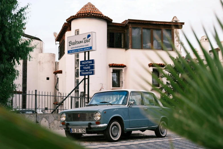 a small blue car parked in front of a building, near the sea, restomod, can basdogan, platinum