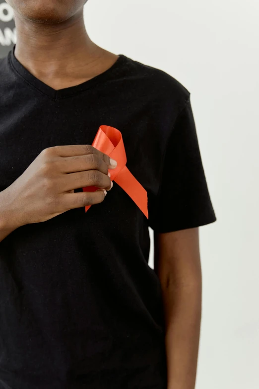 a boy in a black shirt holding a red ribbon, wearing an orange t shirt, zoomed out, disease, non-binary