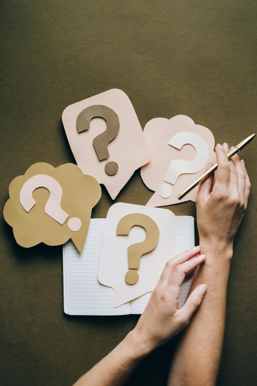 a person writing on a notebook with question marks on it, by Carey Morris, trending on pexels, modernism, paper cutouts of plain colors, etsy, scientific photo, various items