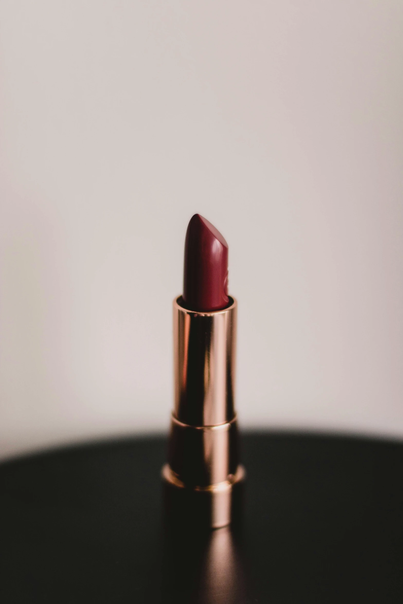 a red lipstick sitting on top of a black table, on a pale background, detailed product image, jovana rikalo, muted brown