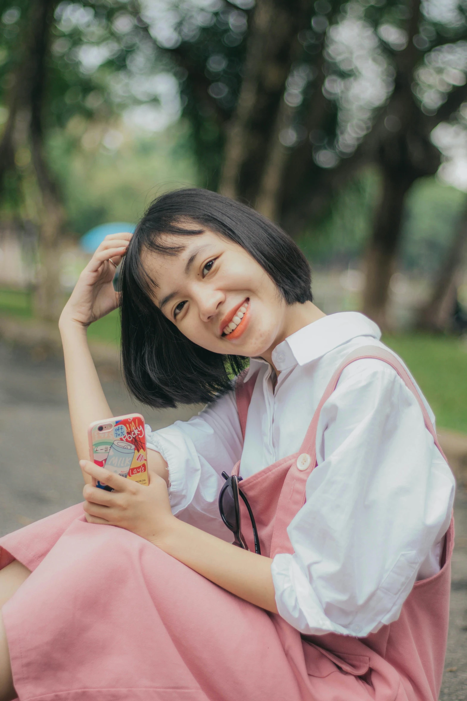a woman sitting on the ground holding a cell phone, by Tan Ting-pho, pexels contest winner, realism, cute slightly nerdy smile, with a bob cut, dang my linh, headshot profile picture