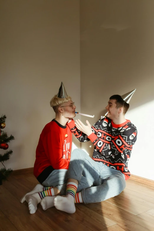 a couple of men sitting on top of a wooden floor, by Julia Pishtar, pexels contest winner, wearing festive clothing, with a cigarette in its mouth, gif, promotional image