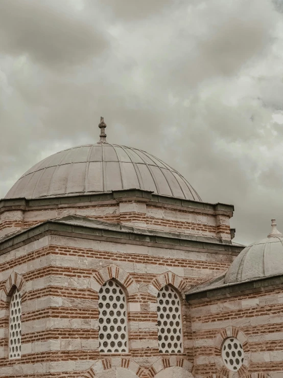 a large building with a clock on top of it, a colorized photo, inspired by Altoon Sultan, pexels contest winner, hurufiyya, rounded roof, black and terracotta, mausoleum, cloudy day