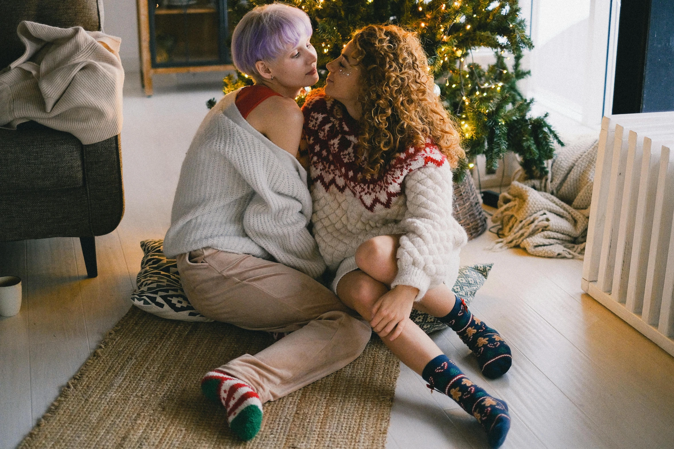 two women sitting on the floor in front of a christmas tree, trending on pexels, lesbian embrace, albino hair, man and woman, wearing a sweater