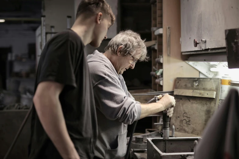 a couple of men standing next to each other in a kitchen, pexels contest winner, arbeitsrat für kunst, scrap metal on workbenches, profile image, old man doing hard work, professional gunsmithing