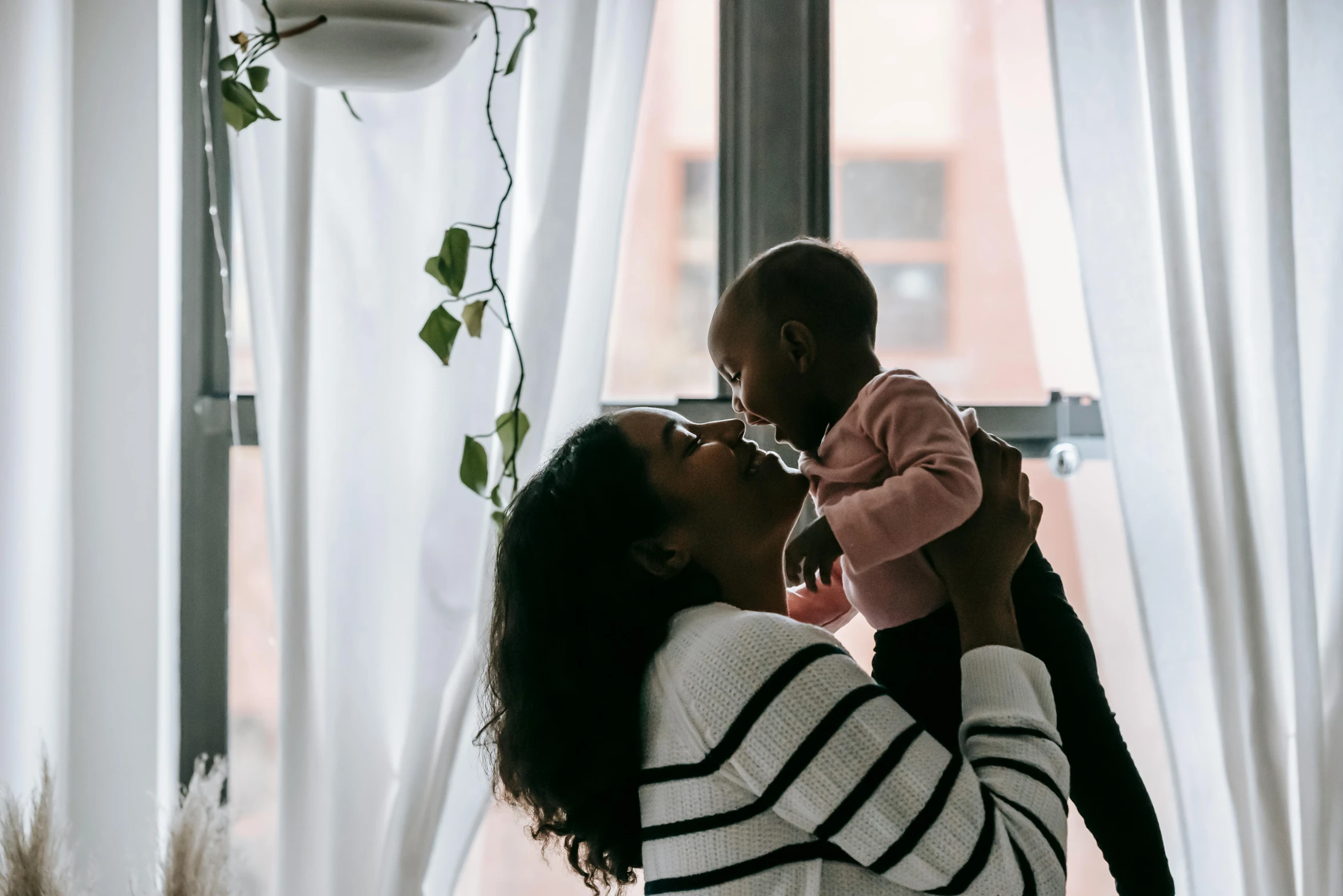 a woman holding a baby in front of a window, pexels contest winner, hurufiyya, varying ethnicities, manuka, holding each other, tall and small