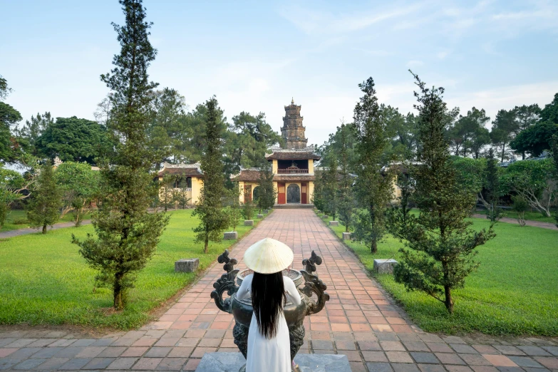 a woman sitting on a bench in a park, inspired by Ruth Jên, pexels contest winner, vietnamese temple scene, ancient tombs in the background, back, sitting on the throne