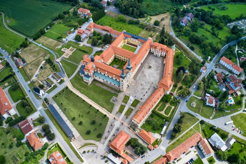 a large building sitting on top of a lush green field, by Adam Marczyński, pexels contest winner, baroque, red roofs, prison complex, square, fpv