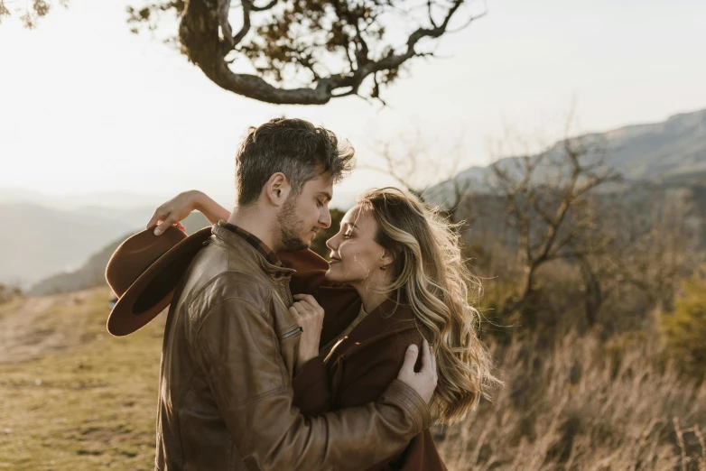 a man and woman standing next to each other in a field, trending on pexels, romanticism, wearing a brown leather coat, avatar image, hollister ranch, on a tree