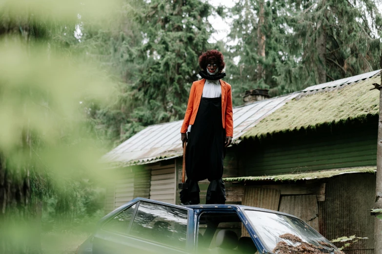 a woman standing on top of a car, by Julia Pishtar, pexels contest winner, afrofuturism, slenderman in the woods, black and orange coat, in front of the house, in style of heikala