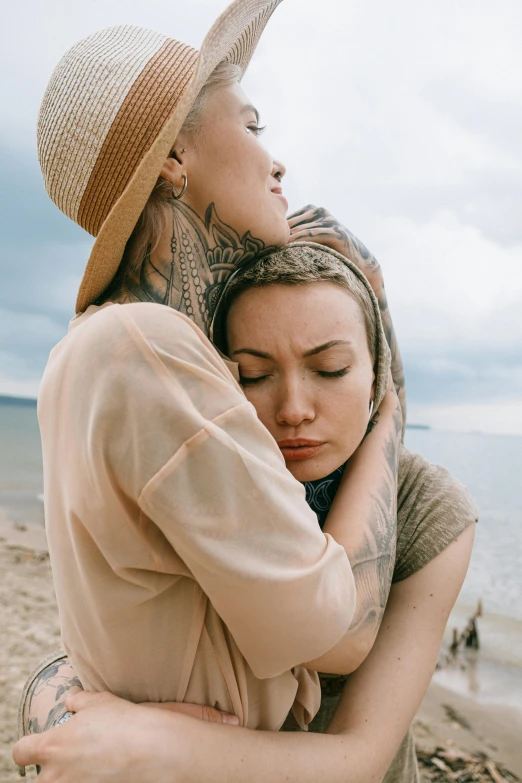 two women hugging each other on the beach, a tattoo, by Matija Jama, trending on pexels, renaissance, covered head, sad expression, androgynous person, high quality image