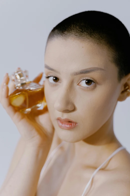 a woman holding a bottle of perfume in front of her face, inspired by Tang Di, unsplash, renaissance, square facial structure, kiko mizuhara, wearing honey, chun - li