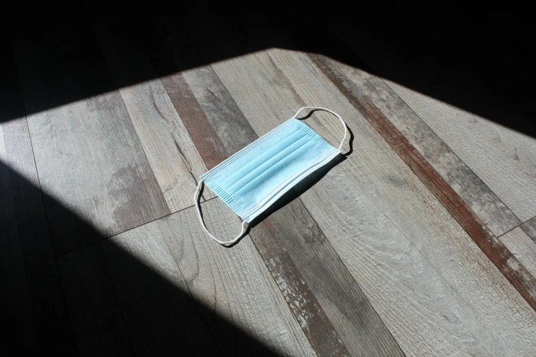 a blue face mask sitting on top of a wooden floor, pexels, contre jour, sitting at the table, rectangle, drop shadow