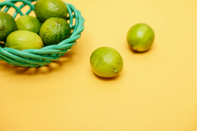 a basket filled with limes sitting on top of a table, by Bertram Brooker, pexels, on a yellow canva, glossy surface, thumbnail, background image