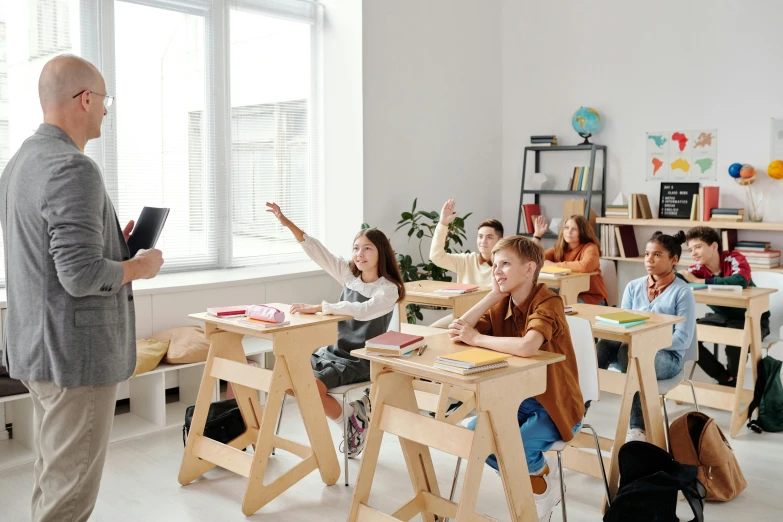 a man standing in front of a classroom full of children, trending on pexels, studying in a brightly lit room, sitting on top a table, clean and simple design, olga buzova