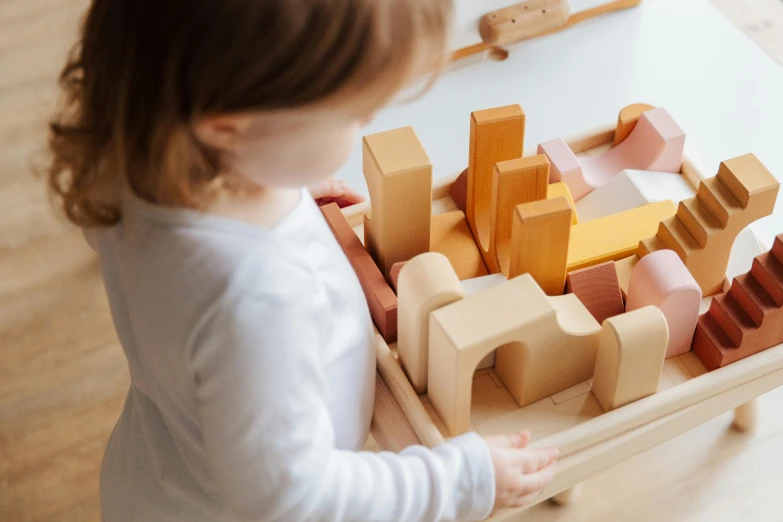 a little girl is playing with a wooden toy, inspired by Rachel Whiteread, pexels contest winner, carrying a tray, urban planning, jovana rikalo, embedded with gemstones