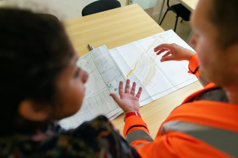 two people sitting at a table looking at a map, a cartoon, pexels, arbeitsrat für kunst, wearing hi vis clothing, civil engineer, close-up photo, nursing