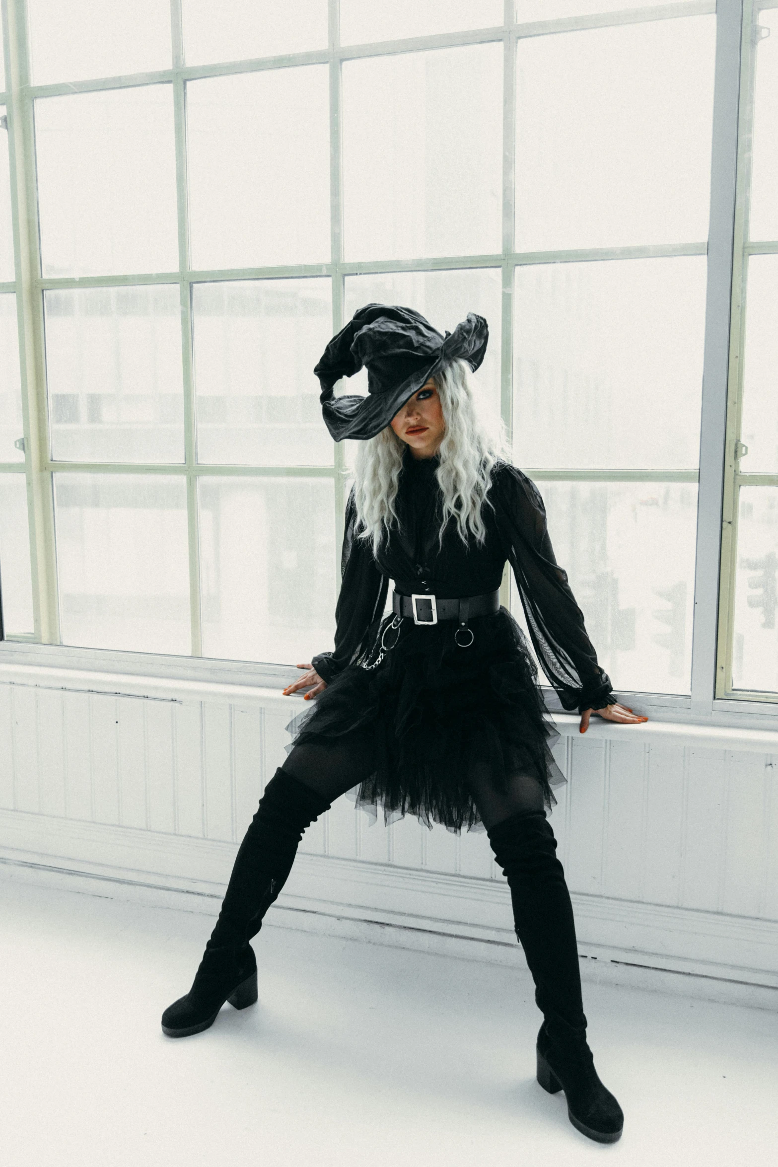 a woman in a witch costume sitting on a window sill, an album cover, trending on pexels, white haired, black hat, full body pose, lulu chen