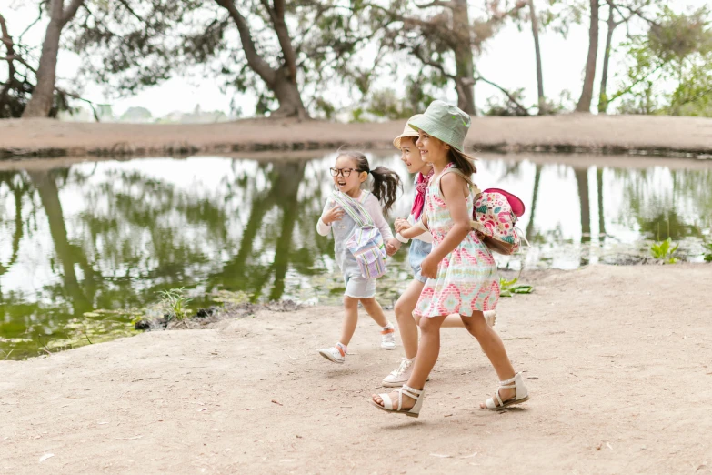 a group of children walking next to a body of water, two girls, modelling, with a backpack, toddler