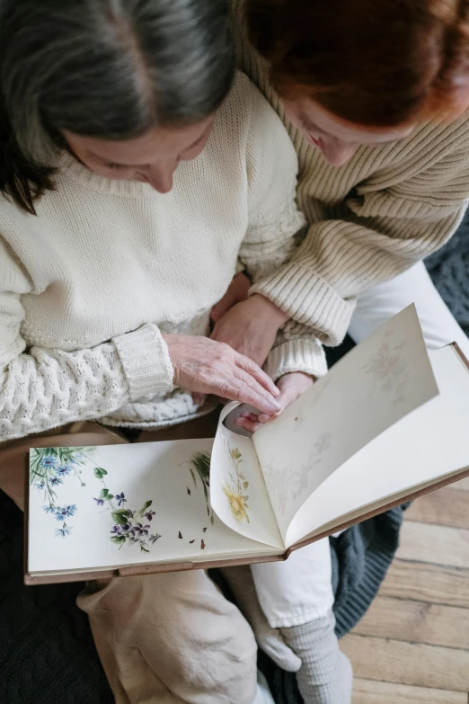 a couple of women sitting on top of a wooden floor, trending on pexels, process art, on a botanical herbarium paper, an elderly, album, an open book