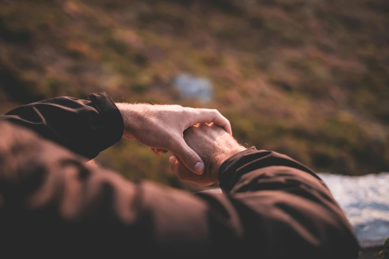 a close up of a person holding a person's hand, a picture, by Jesper Knudsen, unsplash, fan favorite, two men hugging, landscape vista, laying down with wrists together