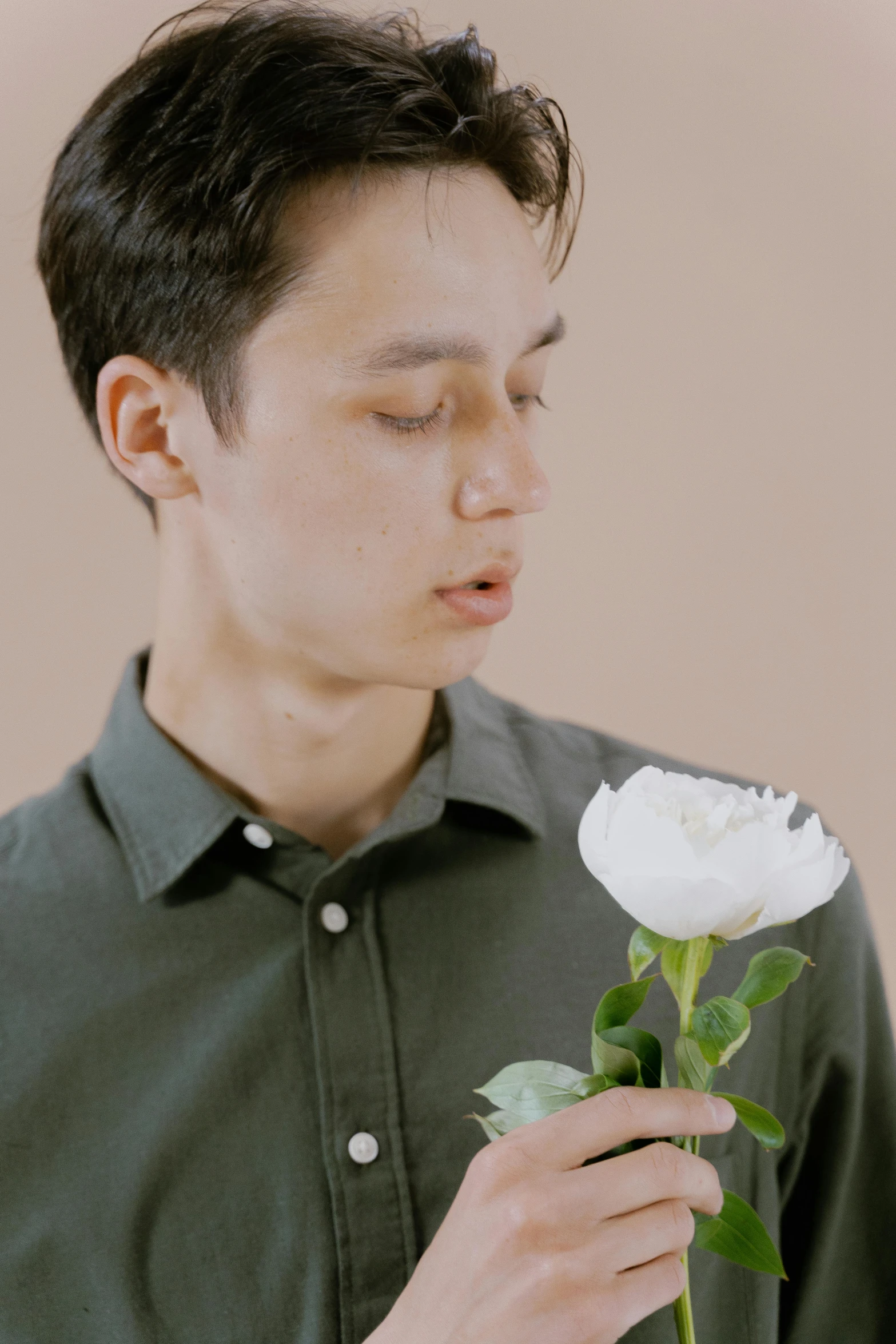 a man in a green shirt holding a white rose, inspired by Jean Malouel, trending on unsplash, non binary model, low quality footage, ignant, flower face