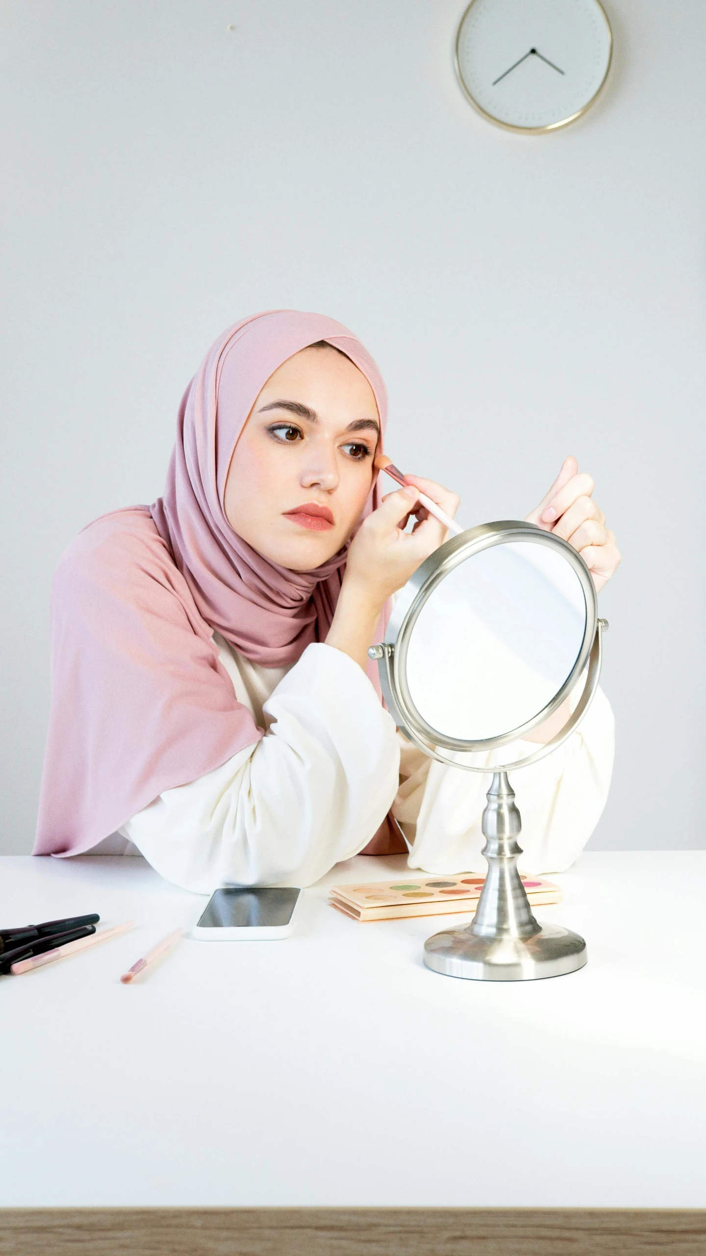 a woman sitting at a table in front of a mirror, by Basuki Abdullah, trending on pexels, hurufiyya, pastel makeup, hijab, set against a white background, product introduction photo