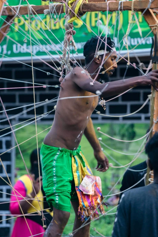 a man standing on top of a wooden structure, wrapped in wires and piones, papa legba, zoomed in, community celebration