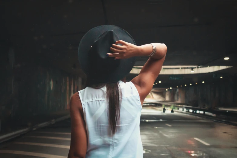 a woman standing in a tunnel with a hat on her head, pexels contest winner, showing her shoulder from back, instagram post, street pic, faded fedora