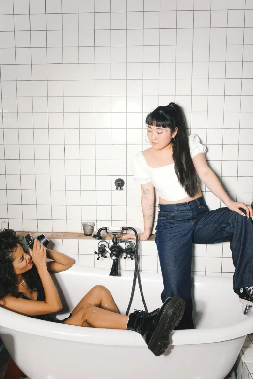 a woman taking a picture of another woman in a bathtub, an album cover, trending on unsplash, half asian, jeans, hot topic, overalls