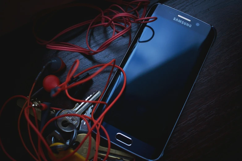 a cell phone sitting on top of a wooden table, by Adam Marczyński, trending on pexels, process art, red headphones, attached to wires. dark, complicated circuits and wires, avatar image