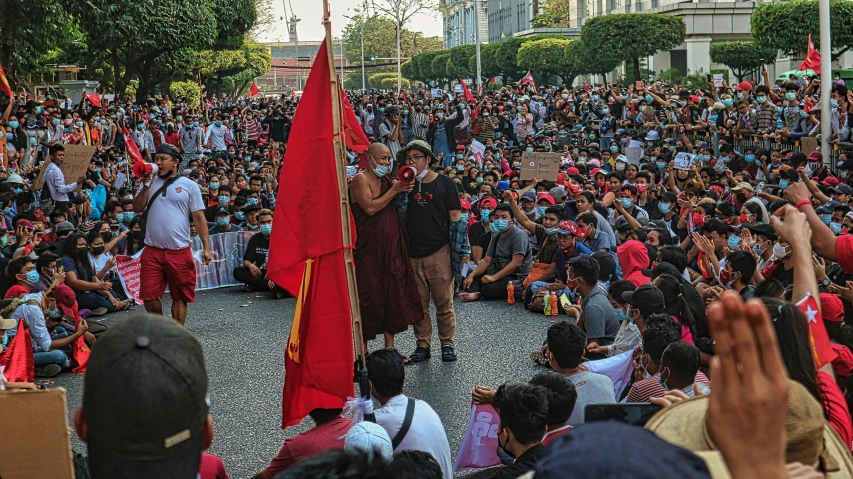 a group of people that are standing in the street, red and black flags, sitting down, raden saleh, maroon