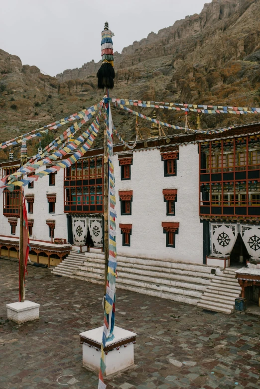 a group of flags hanging from a pole in front of a building, tibetan inspired architecture, white wall complex, monastery, black