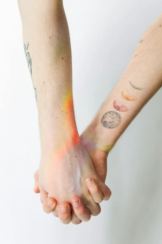 a close up of two people holding hands, a tattoo, by Jessie Alexandra Dick, light and space, broken rainbow, lunar color palette, promo image, synthetic bio skin