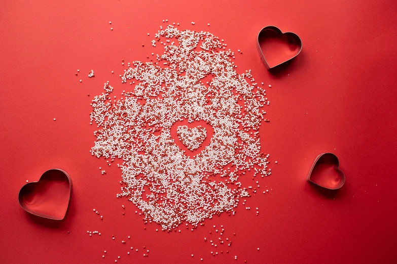 a heart made out of sugar sprinkles on a red background, by Julia Pishtar, visual art, background image, silver，ivory, scattered props, gypsophila