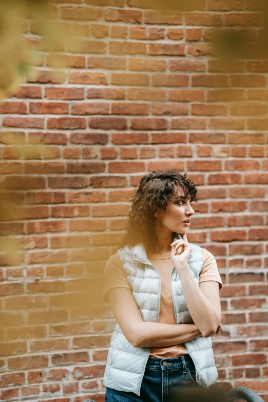 a woman standing in front of a brick wall, inspired by Elsa Bleda, trending on pexels, renaissance, curly bangs, medium format. soft light, pondering, handsome girl