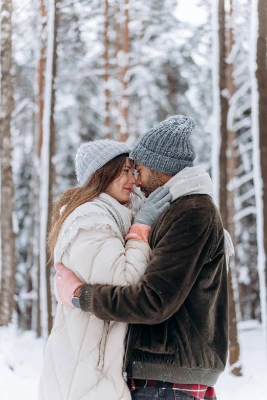 a man and woman standing next to each other in the snow, pexels contest winner, romantic themed, beanie, with trees, grey