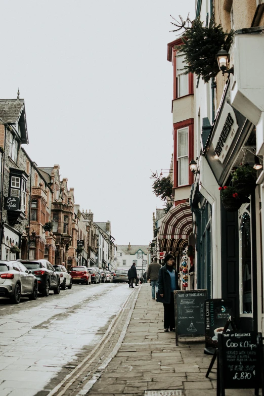 a couple of people that are walking down a street, by Kev Walker, pexels contest winner, arts and crafts movement, beautiful small town, cars parked underneath, upon a peak in darien, wet streets