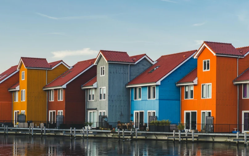 a row of colorful houses next to a body of water, by Jan Tengnagel, pexels contest winner, modernism, cottages, industrial colours, concept photo, thumbnail