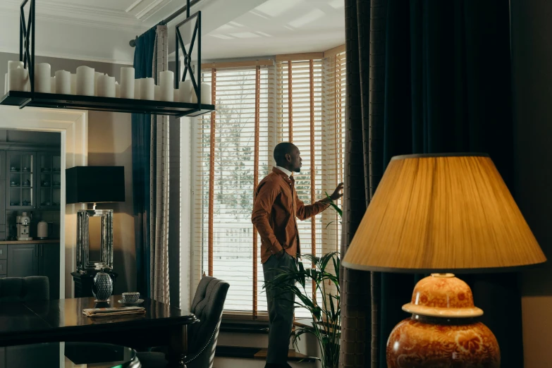 a man standing in a living room next to a lamp, by Julia Pishtar, pexels contest winner, luxurious environment, looking in the window, tv commercial, beaded curtains