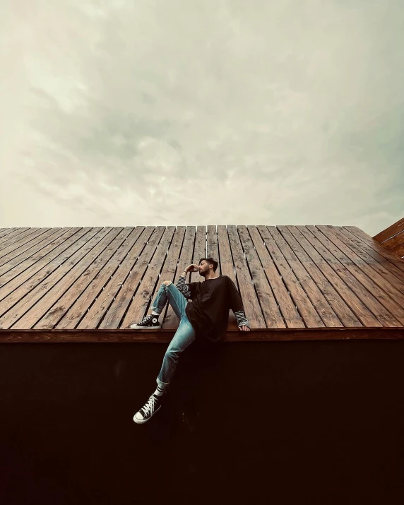 a man sitting on top of a wooden roof, a picture, trending on pexels, lgbtq, alternate album cover, deep in thought, low quality photo