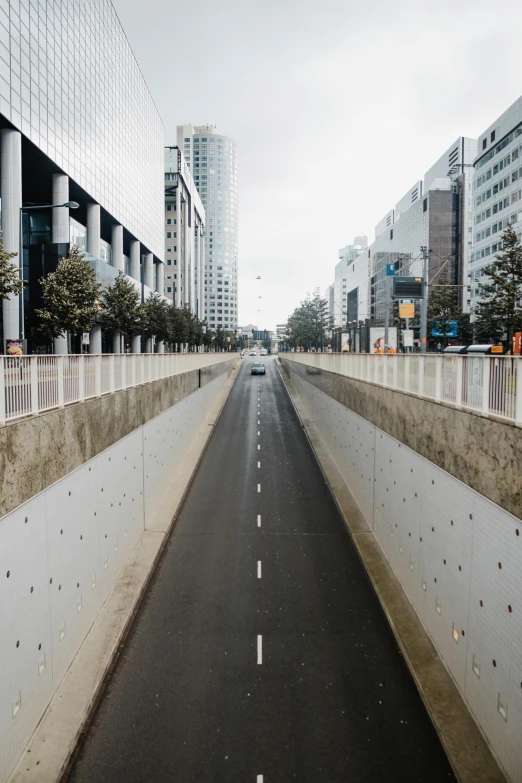 a car driving down a street next to tall buildings, inspired by Thomas Struth, unsplash, high walled tunnel, neotokyo, empty road in the middle, belgium