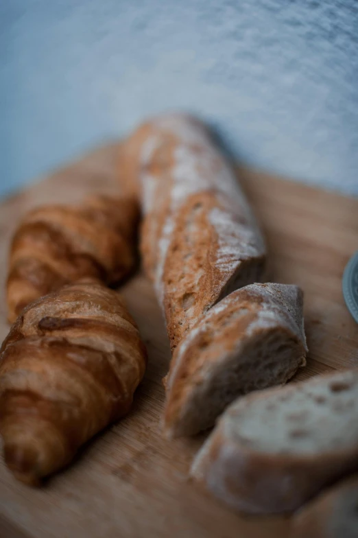 a couple of croissants sitting on top of a wooden cutting board, a portrait, unsplash, baking french baguette, 2995599206, high angle close up shot, brown bread with sliced salo